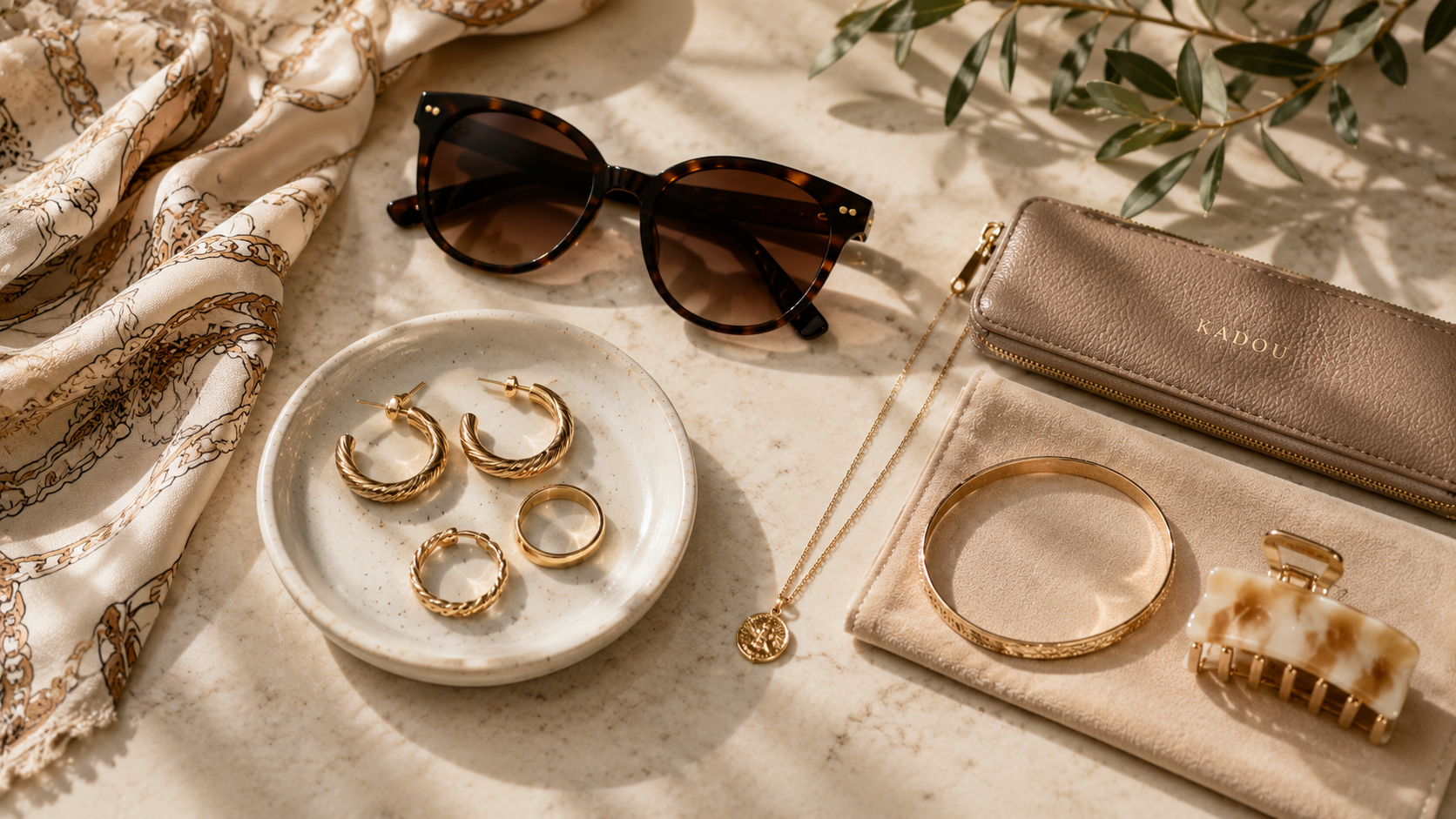 Women’s accessories styled with sunglasses, gold jewelry, scarf, and leather pouch at KADOU Boutique