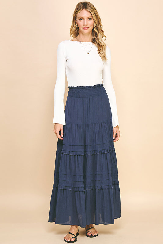 The model is wearing the Tiered Maxi Skirt in dusty navy color with a white top.