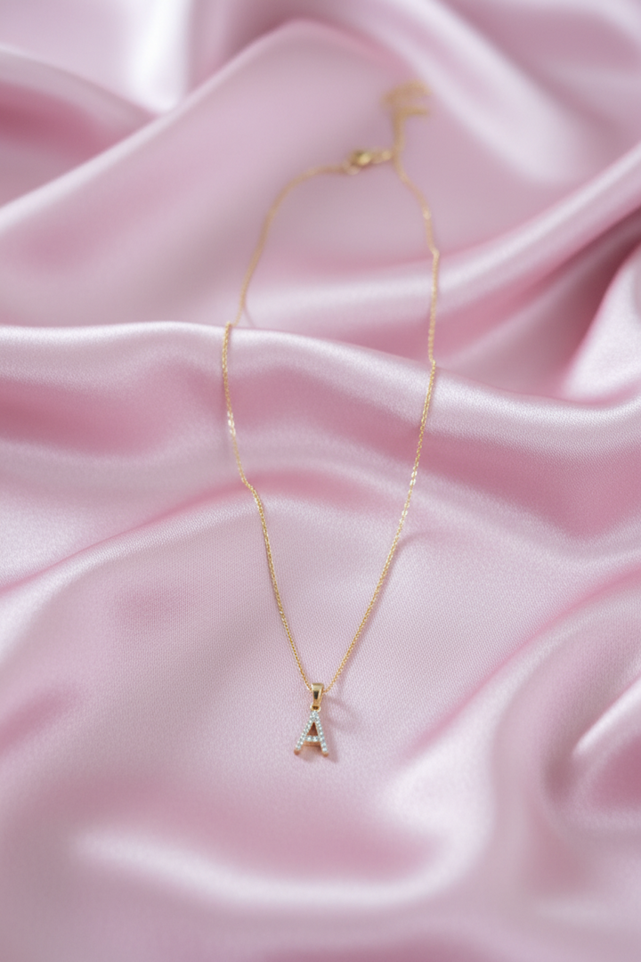A delicate gold necklace with a letter &