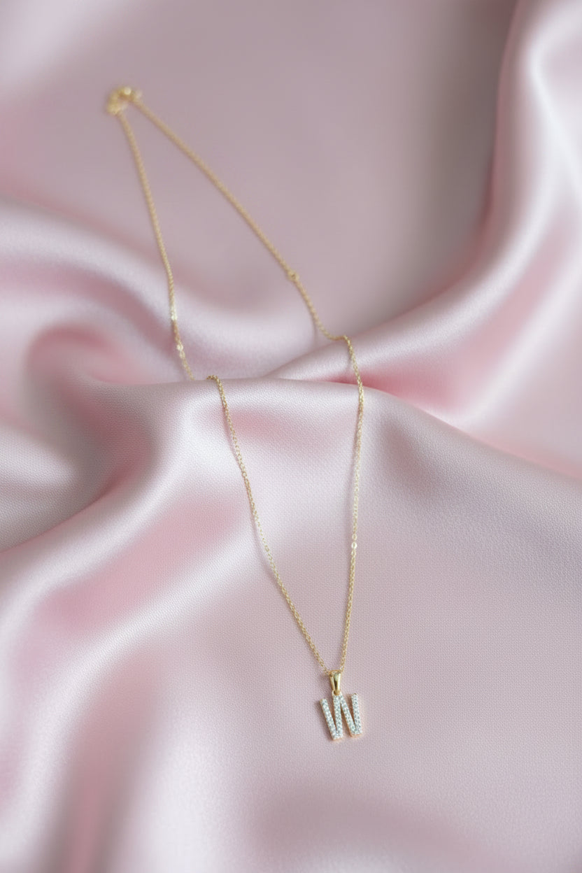 A delicate gold chain necklace with a small initial pendant spelling &