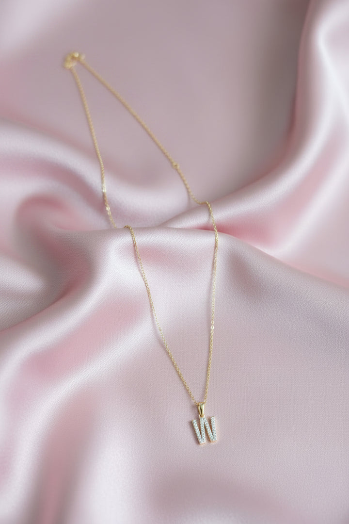 A delicate gold chain necklace with a small initial pendant spelling &