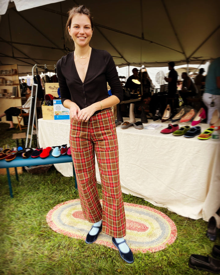Woman in plaid pants standing in front of a shoe display under a tent.
