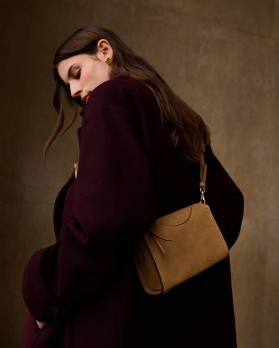 Woman holding a brown handbag against a brown background