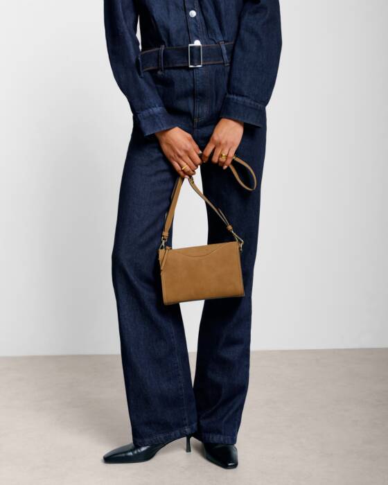 Person wearing a denim outfit holding a brown handbag against a plain background