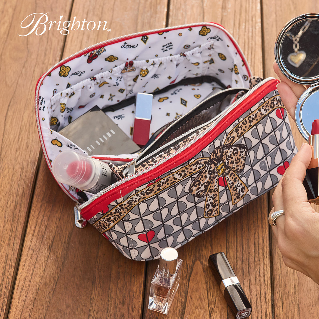 Patterned makeup bag with cosmetic items on a wooden surface, featuring the Brighton brand.