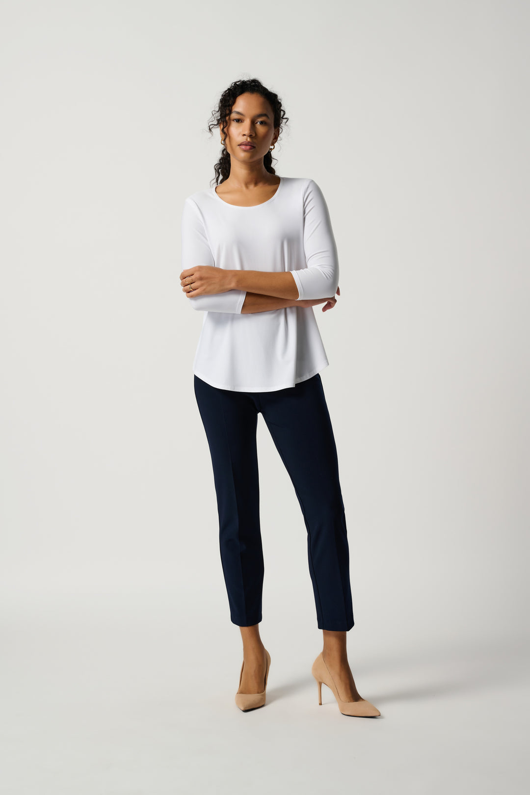 Woman wearing a white top and navy pants on a light gray background