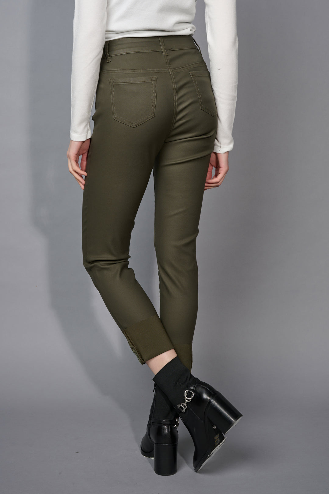 A back view of a person wearing olive green pants and black boots on a gray background
