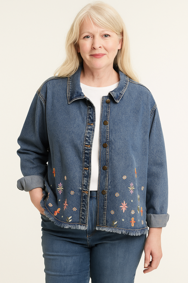 Woman wearing a blue denim jacket with floral embroidery on a plain background
