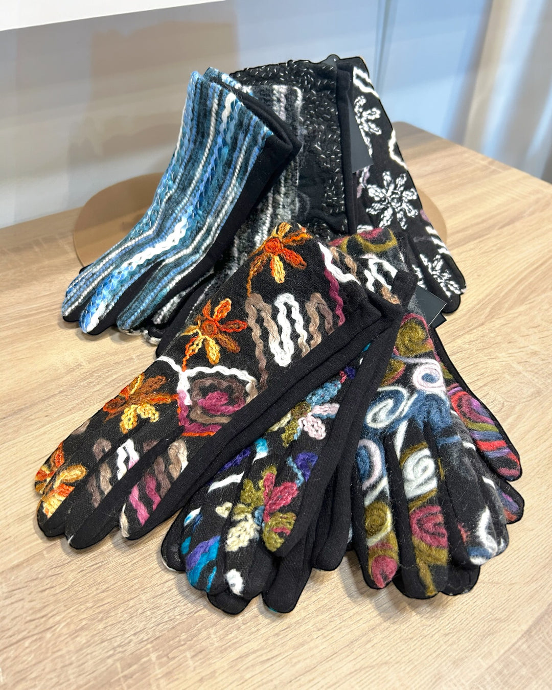 Pair of black gloves with colorful floral patterns on a wooden surface