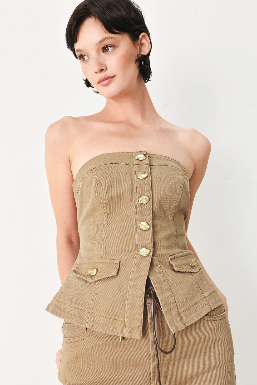 Woman wearing a strapless beige jacket with button details on a white background