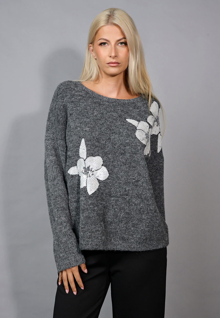 Woman wearing a gray sweater with floral patterns on a gray background