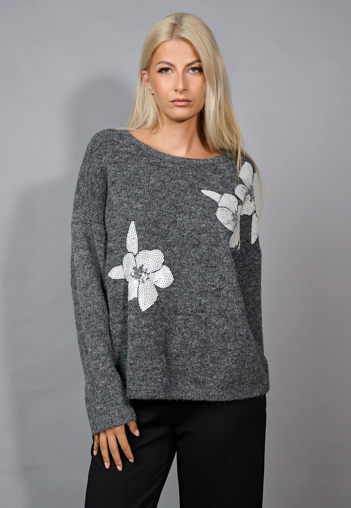 Woman wearing a gray sweater with floral patterns on a gray background