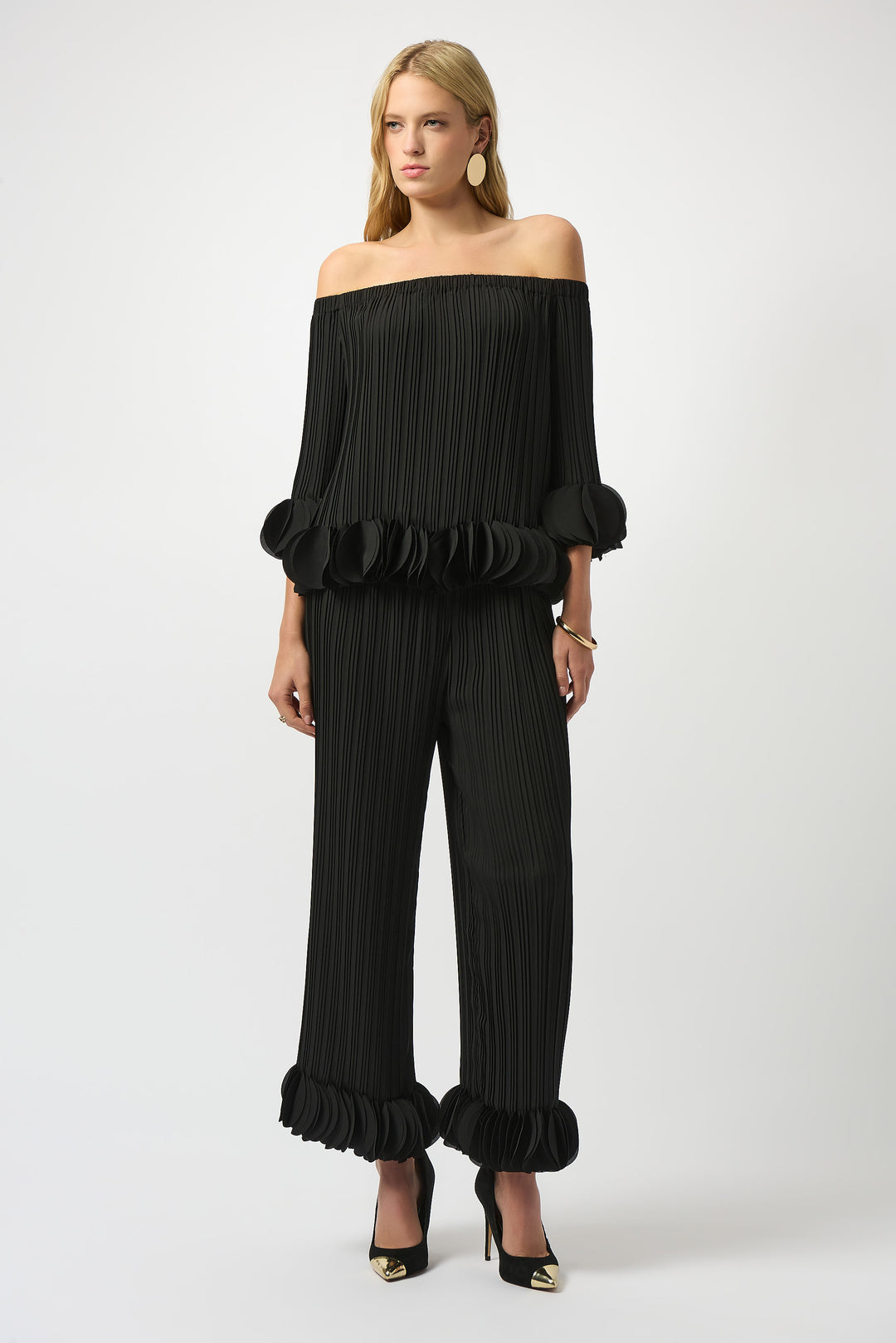 Woman wearing a black off-shoulder top and wide-leg pants on a white background