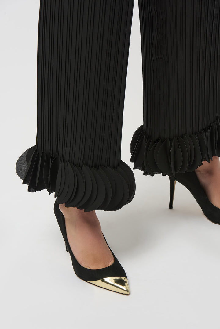Black pleated pants with ruffled cuffs worn with black high-heeled shoes on a white background