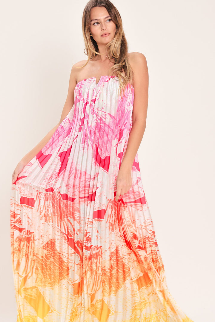 Woman wearing a strapless, tie-dye dress with pink, white, and orange colors on a plain background.
