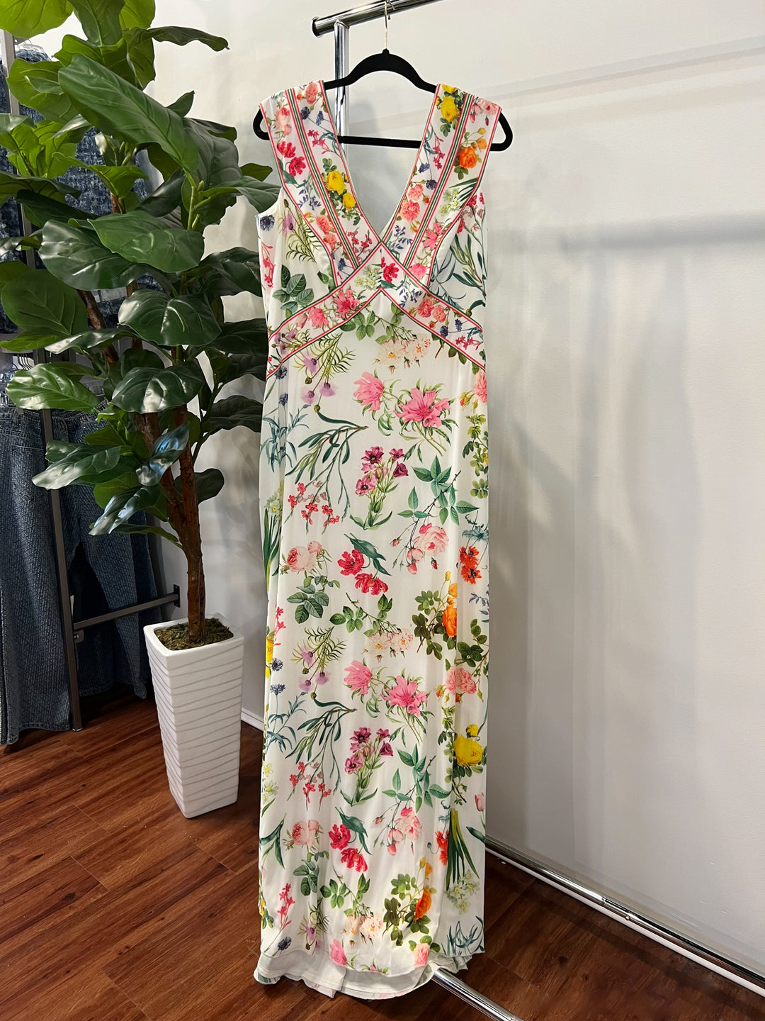Floral dress hanging on a rack with a plant and white wall in the background