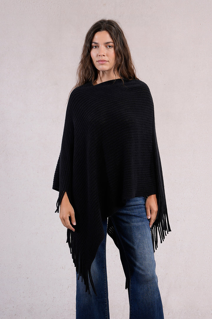 Woman wearing a black poncho with fringe details on a plain background