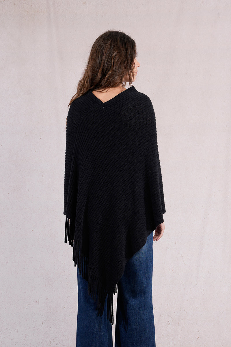 Person wearing a black poncho with fringes on a plain background