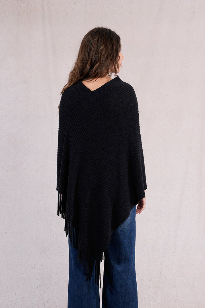 Person wearing a black poncho with fringes on a plain background