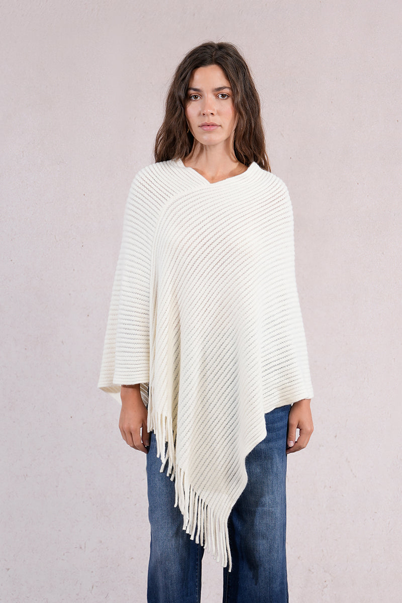 Woman wearing a white poncho with fringe details on a plain background