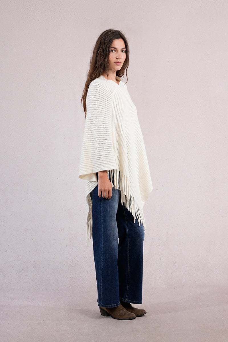 Woman wearing a white poncho and blue jeans on a plain background