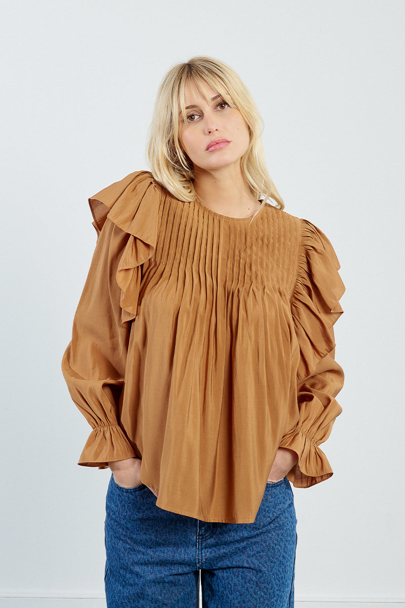 Woman wearing a brown blouse with ruffled sleeves against a white background