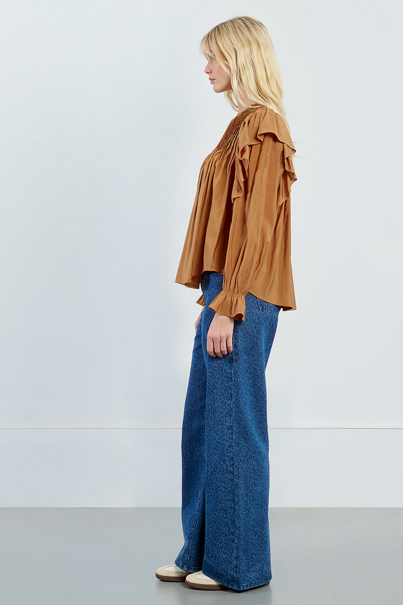 A side view of a woman wearing a brown blouse and blue pants against a white background