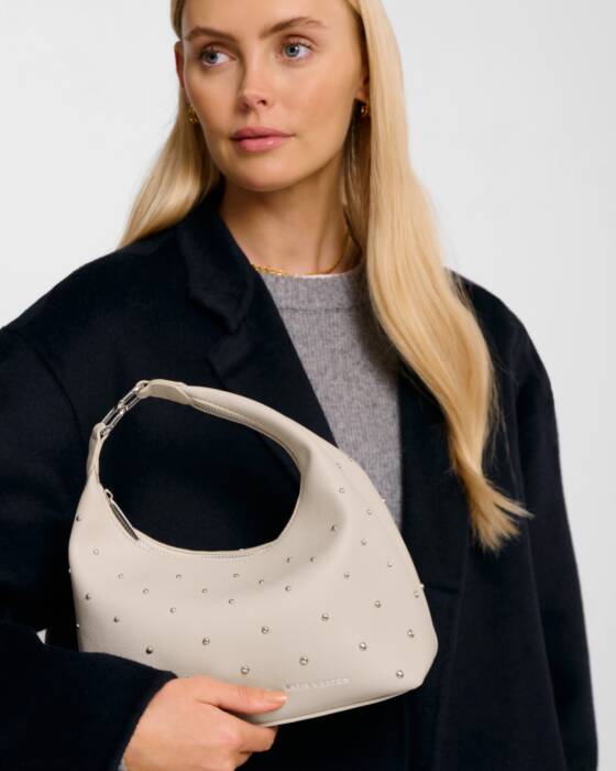Woman holding a beige handbag with decorative studs against a plain background
