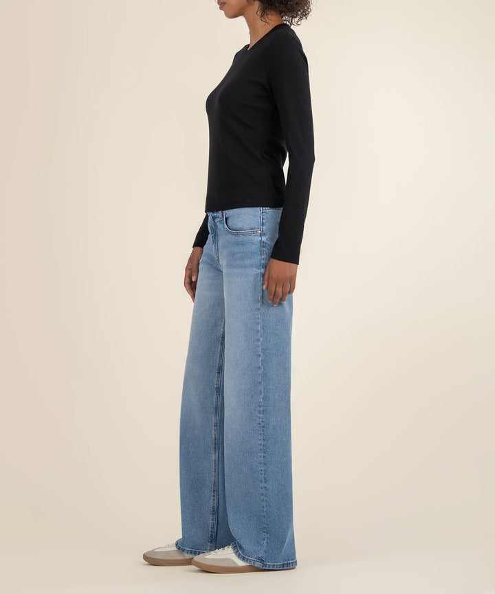 A side view of a person wearing a black long-sleeve top and blue wide-leg jeans on a beige background