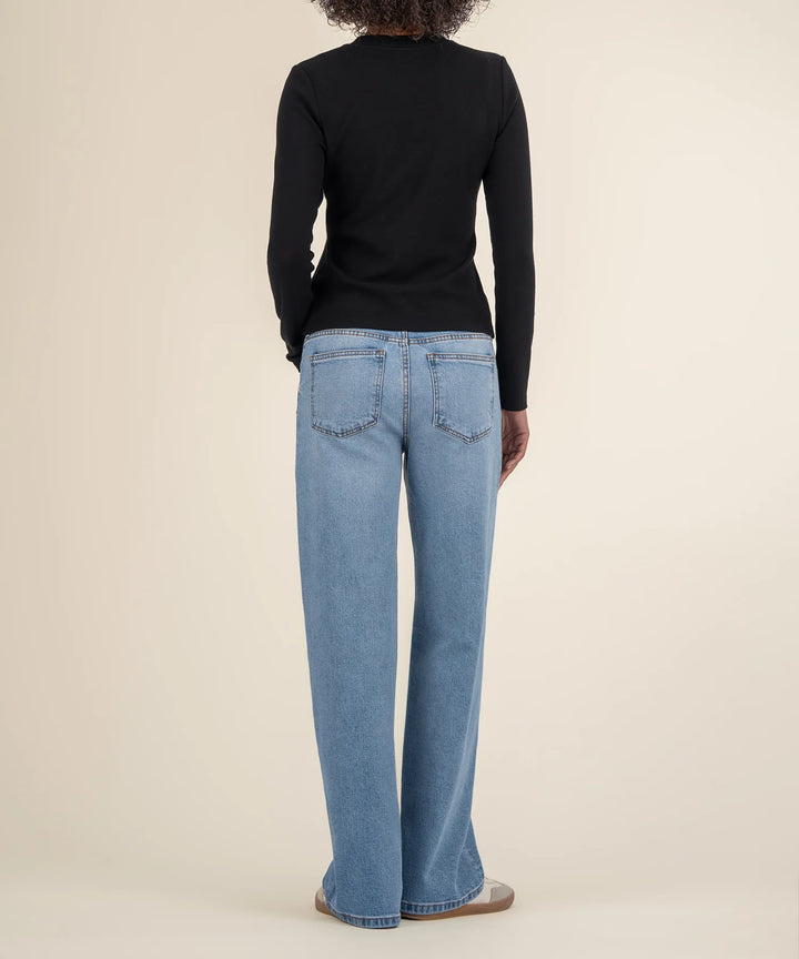 A back view of a person wearing blue jeans and a black top on a beige background