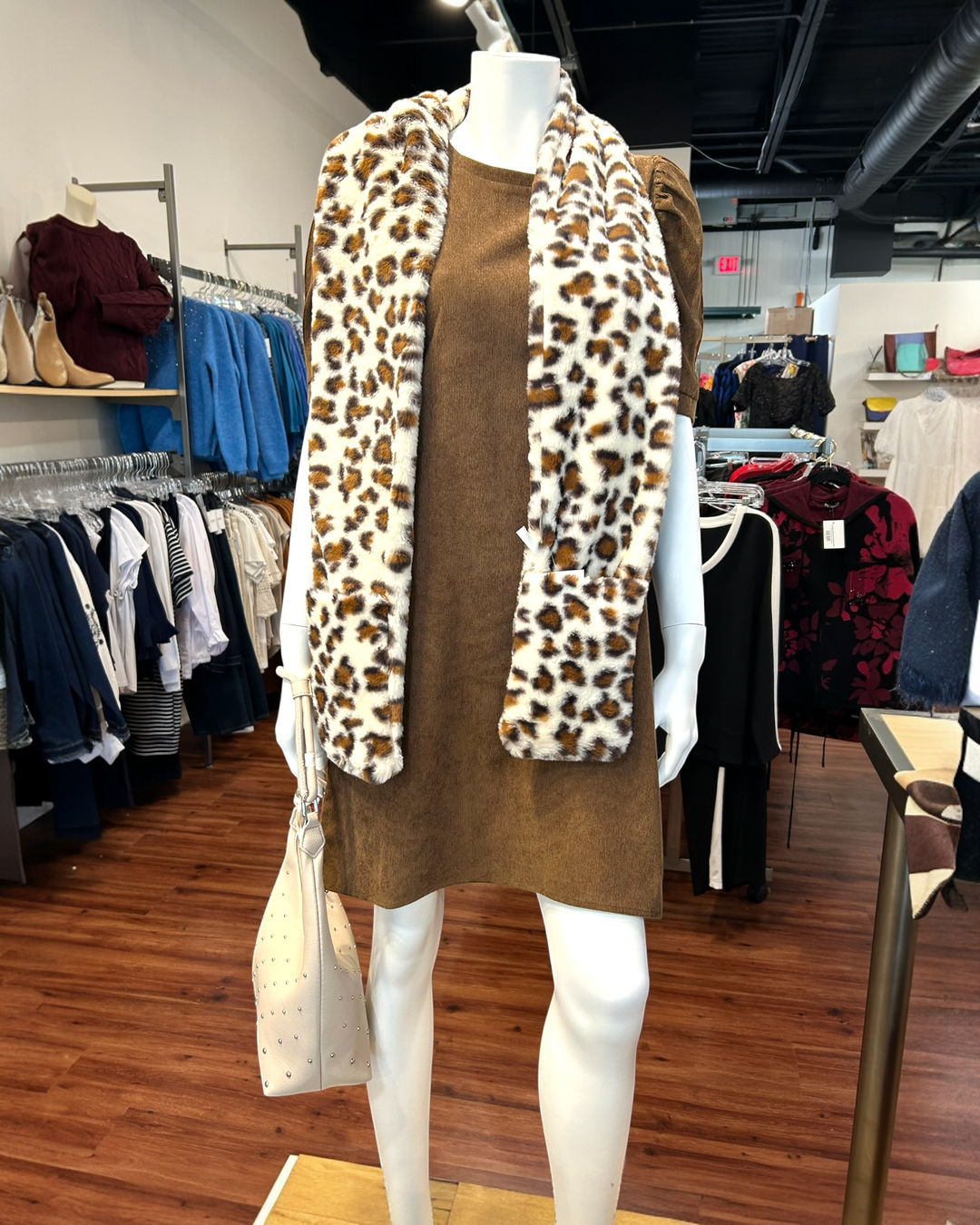 Mannequin wearing a brown dress with a leopard print scarf in a clothing store.