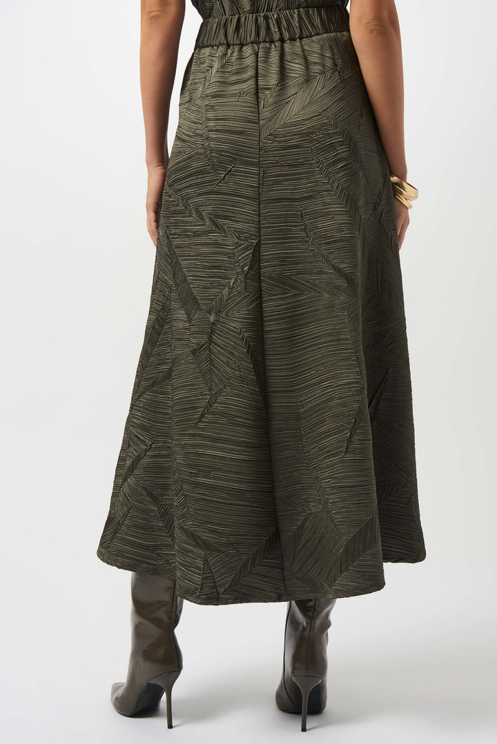 Person wearing a long, patterned green skirt on a white background. A back view.
