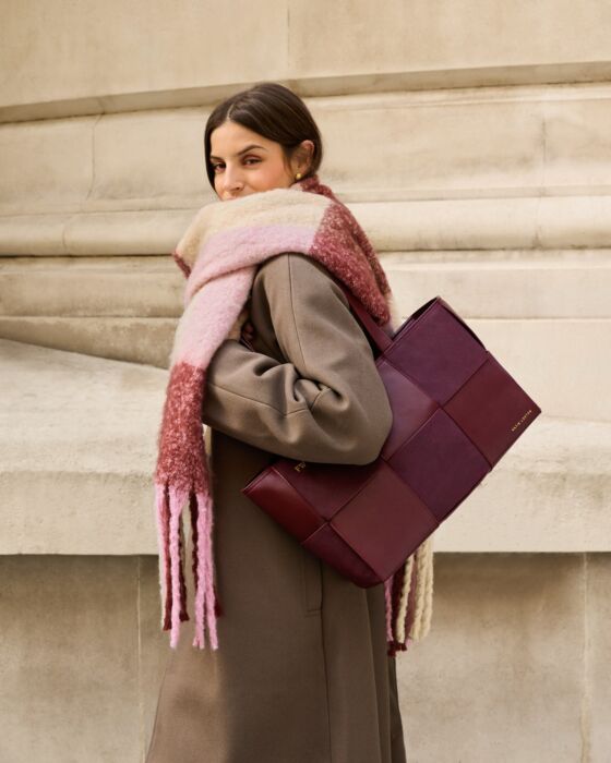 Woman holding a patterned bag and wearing a colorful scarf against a stone wall.