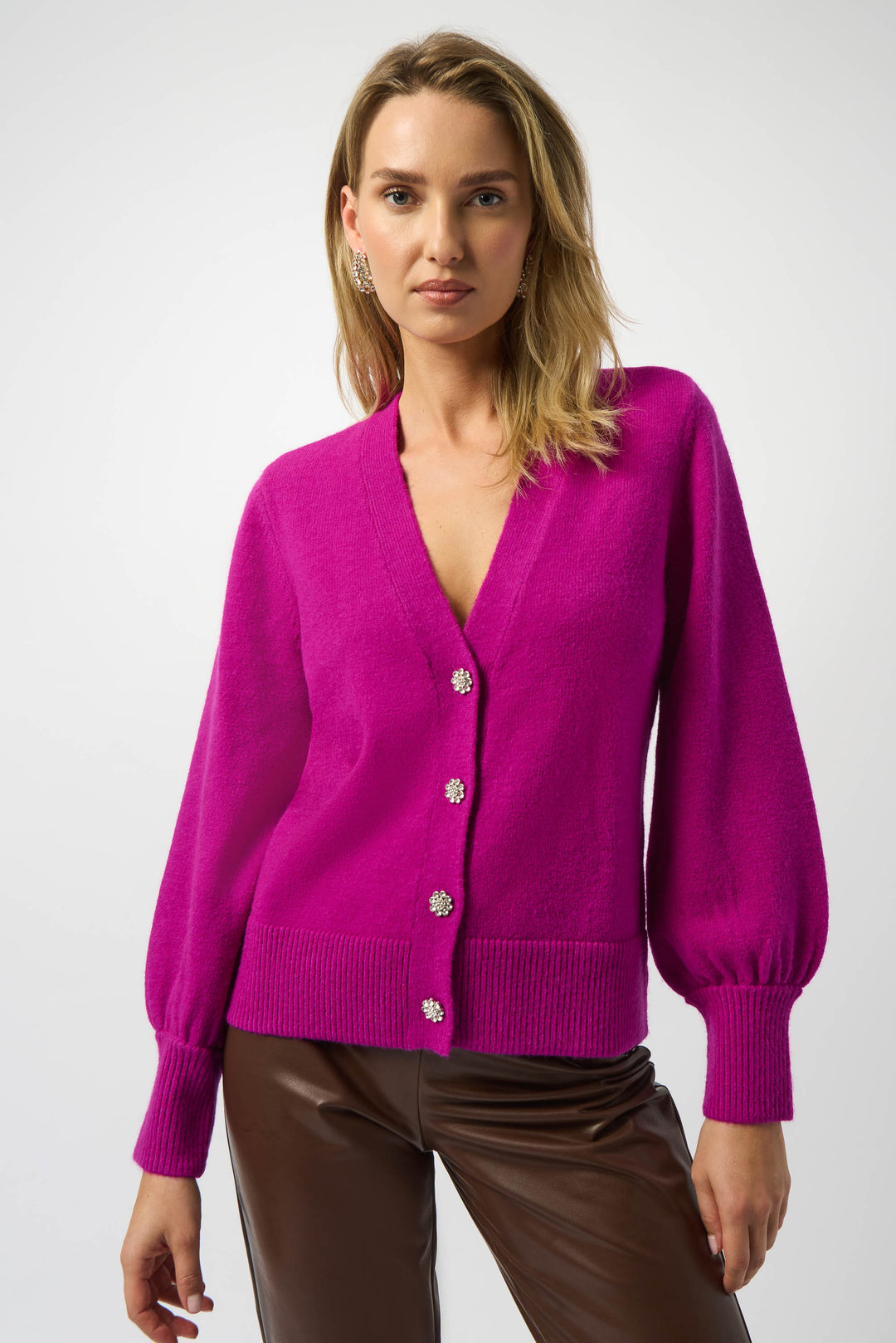Woman wearing a bright pink cardigan with silver buttons on a white background