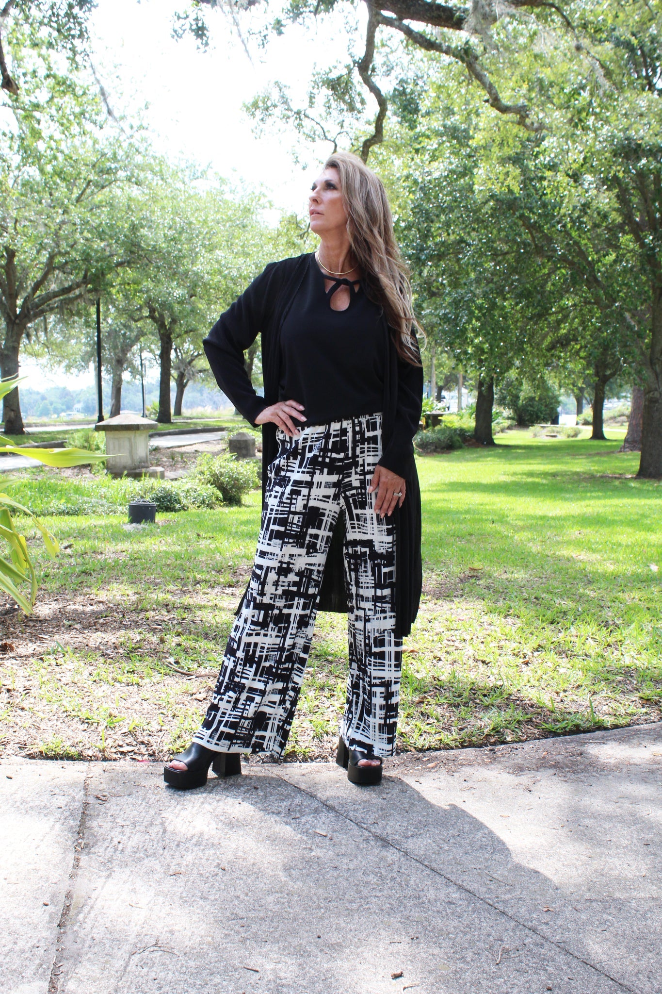 Model wearing the Ribbed Flare Pants in Black/White with black top and long cardigan standing in the park.