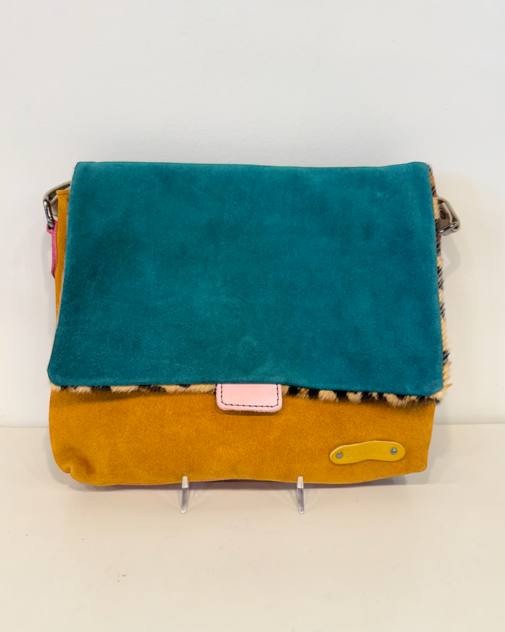 Teal and mustard yellow handbag with a pink patch on a white background