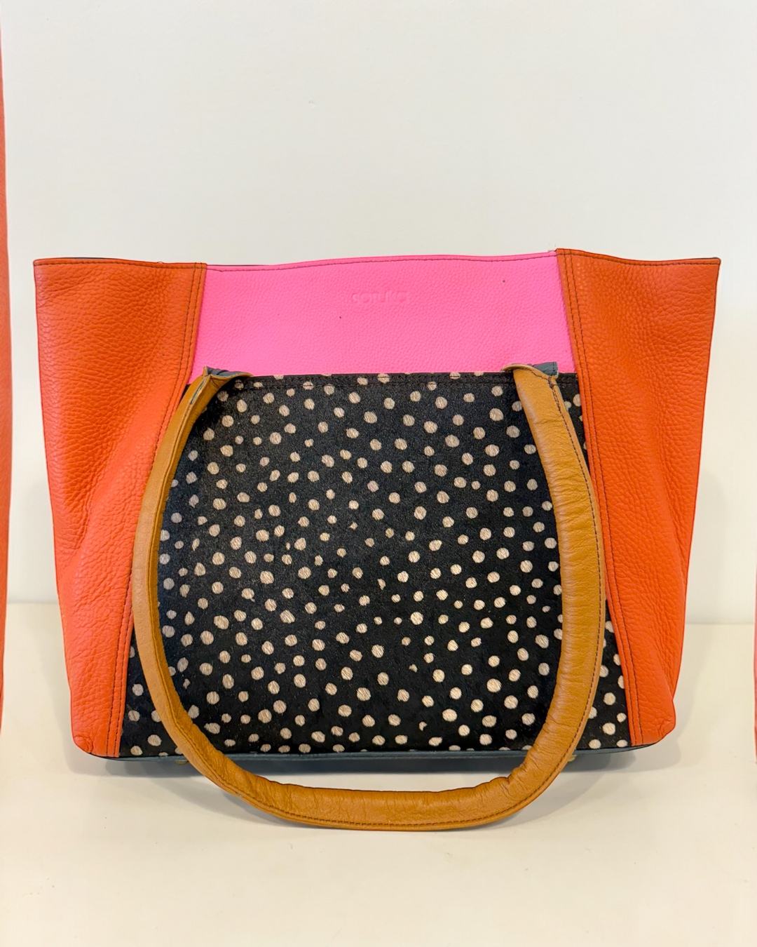 Handbag with orange, pink, and polka dot animal print pattern on a beige background