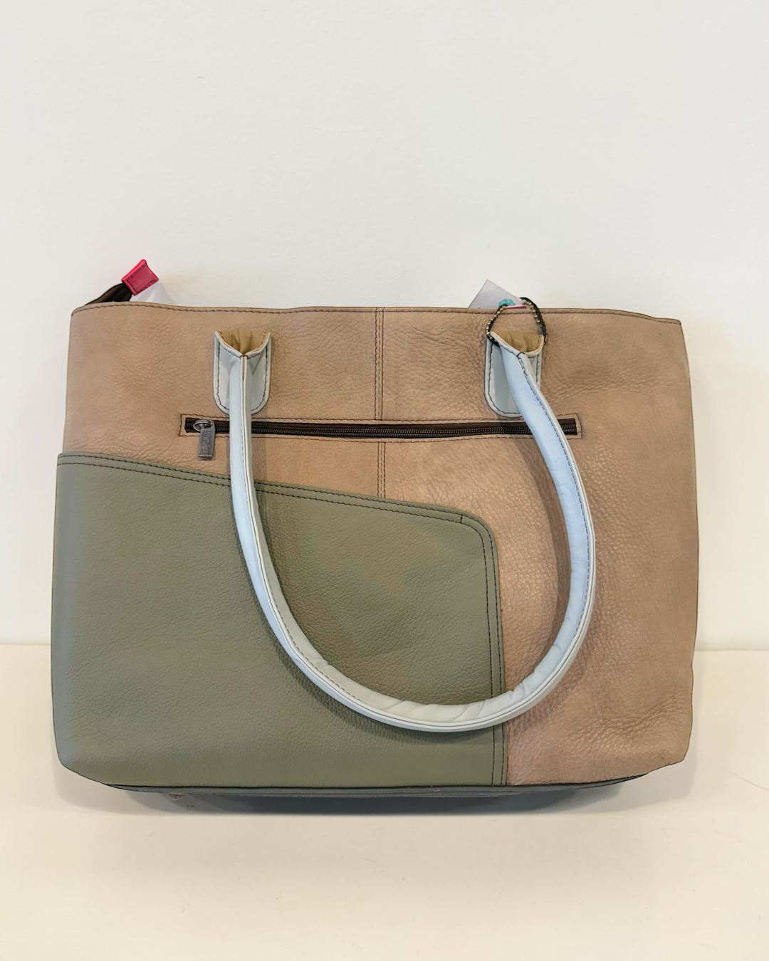 Two-tone beige and green handbag with a light gray handle on a light background