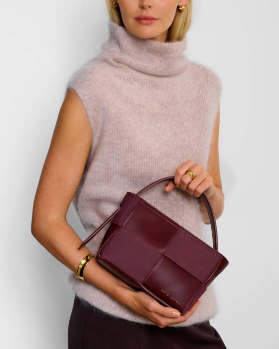 A lady holding a burgundy handbag against a plain background
