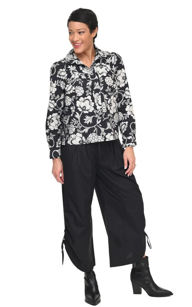 Woman wearing a black and white floral blouse with black pants on a white background