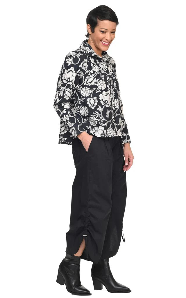 A side look at a woman wearing a black and white patterned shirt with black pants and boots on a white background