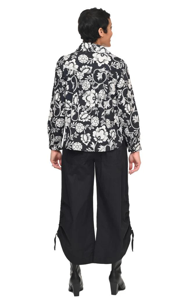 A back view of a woman wearing a black and white floral patterned shirt with wide-leg pants on a white background
