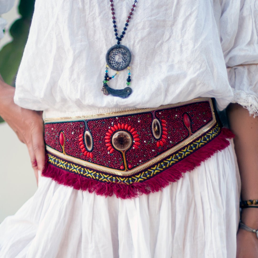The model is wearing the Beaded Stretch Belt in pomegranate red with a white dress. 