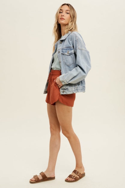 The model is wearing The Denim Jacket with a brick-colored shorts. 