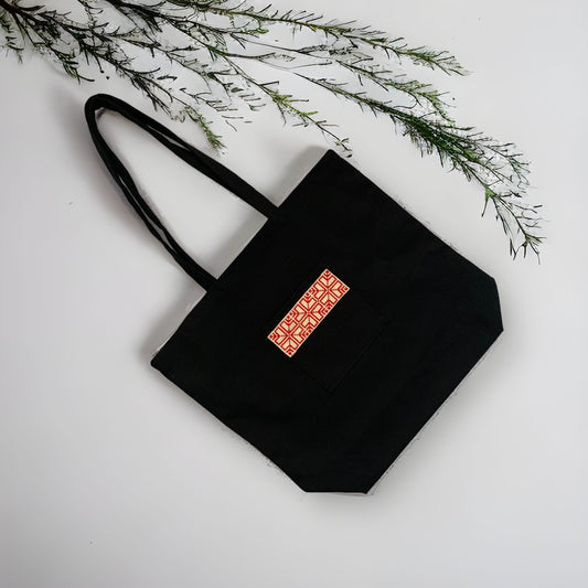 Showing the Tatreez Fabric Tote Bag in Black color and Red embroidery on the outside pocket.Available at Kadou Boutique.