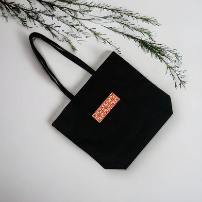 Showing the Tatreez Fabric Tote Bag in Black color and Red embroidery on the outside pocket.Available at Kadou Boutique.